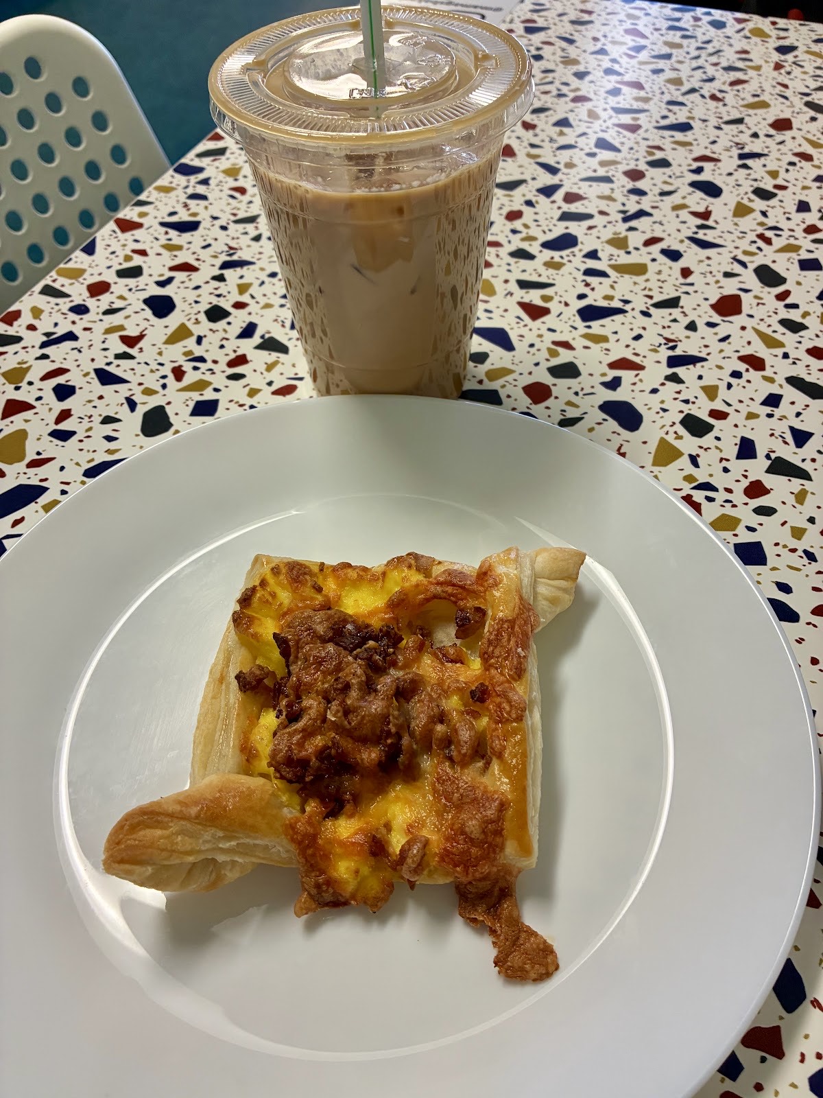 Bacon and egg pastry beside an iced coffee on a colorful table