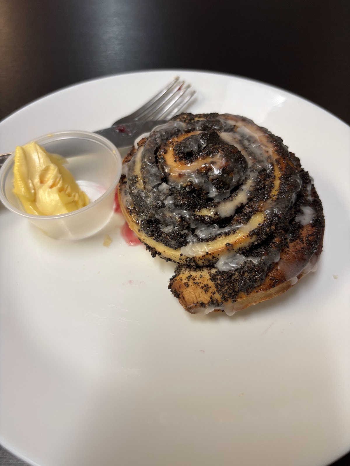 Glazed poppyseed swirl roll on a white plate with butter